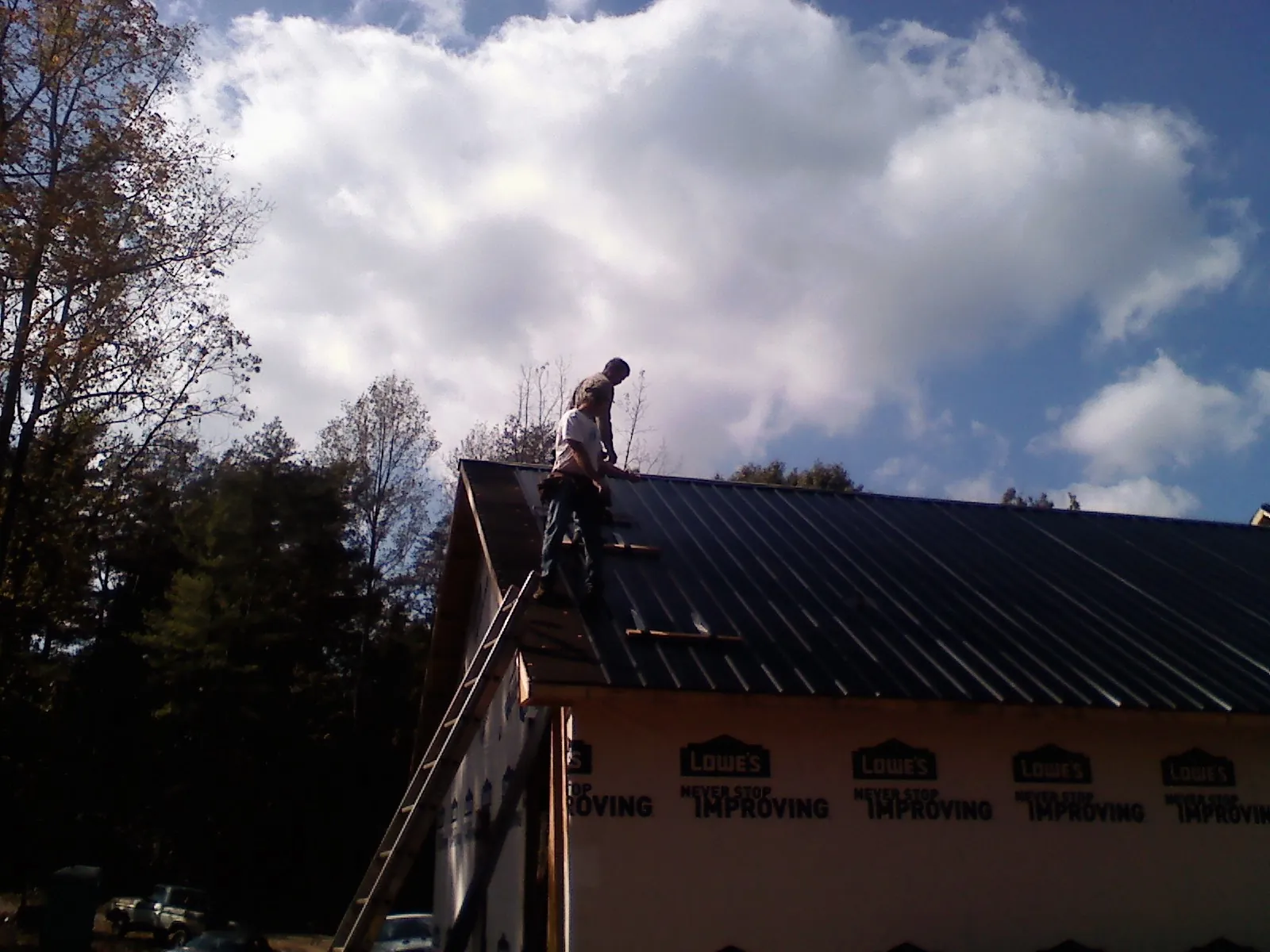 Roofer fastening dark metal panels high against a cloudy sky, from a Roof Inspection job in Jefferson